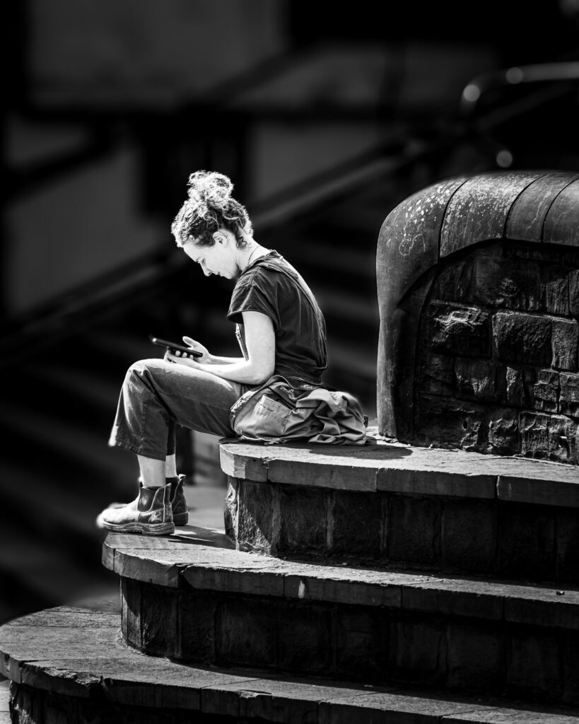 Student sitting on stone steps using smartphone in dramatic natural lighting by MIchael Dutson Landscape Photography