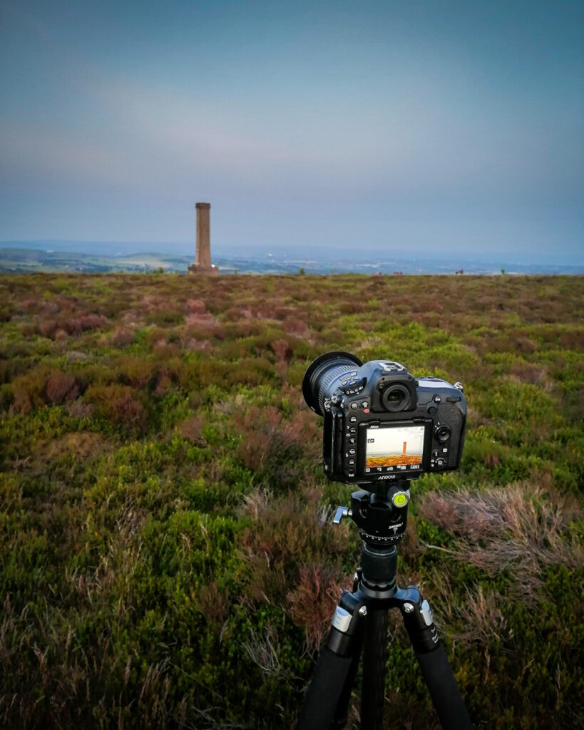 Nikon DSLR camera on tripod positioned on Holcombe Moor with Peel Monument tower visible in distance across moorland heather landscape