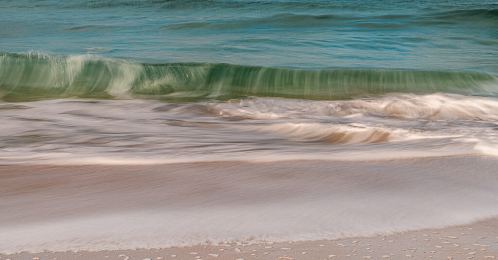 Long exposure photograph of waves breaking on Dail Mor beach, creating smooth, silky motion blur as turquoise and white water flows across golden sand.